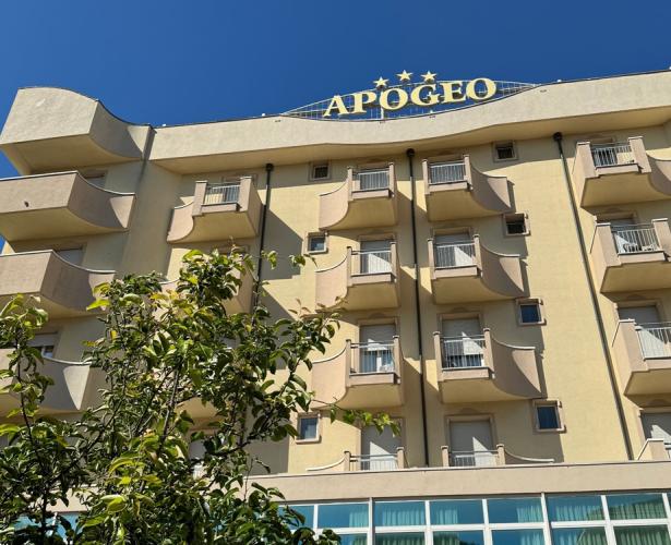 Edificio giallo con balconi e insegna 'APOGEO', cielo blu sullo sfondo.